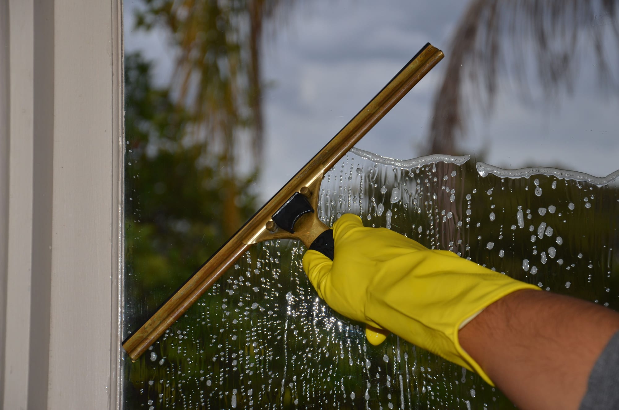 Gebäudereiniger zieht mit gelbem Handschuh eine Glasfassade mit dem Fensterabzieher ab