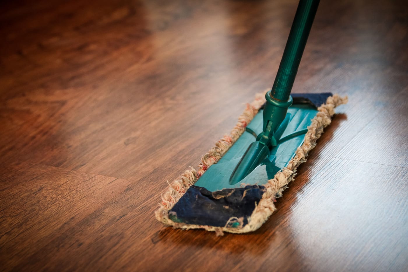 Gebäudereiniger wischt mit dem Flachmopp einen dunklen Holzboden